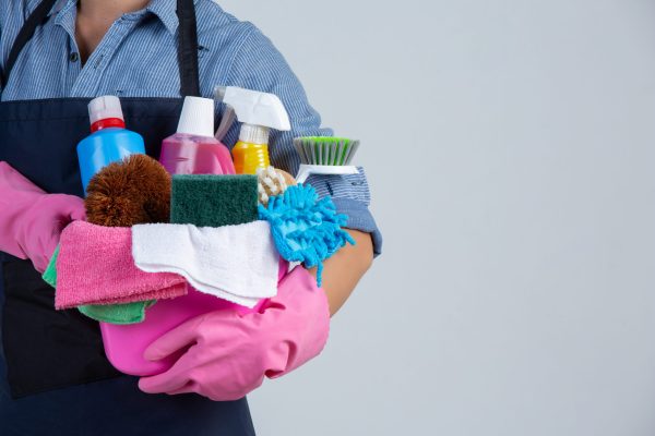 Young girl is holding cleaning product, gloves and rags in the b Young girl is holding cleaning product, gloves and rags in the basin on white background